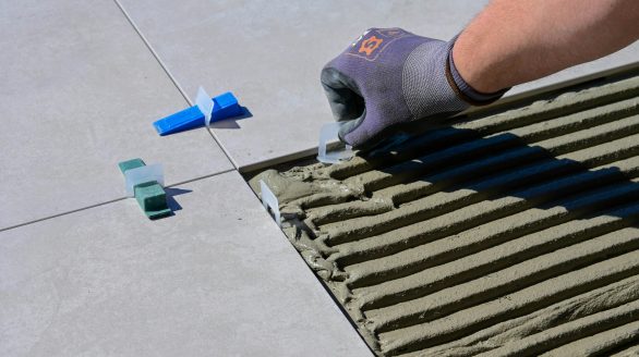 Detailed view of gloved hand aligning tiles with levelers and spacers during construction.